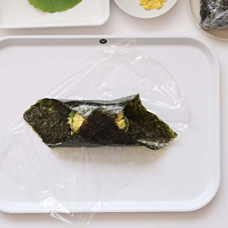 김 모서리를 안으로 접고, 랩으로 단단히 타원형 모양으로 감싸 2등분으로 잘라주세요.
