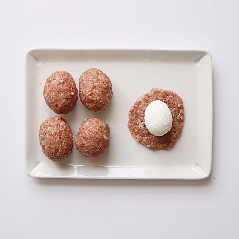 고기반죽을 동글 납작하게 펴준 후, 밀가루 묻힌 삶은 달걀을 넣어 동그란 모양으로 감싸주세요.