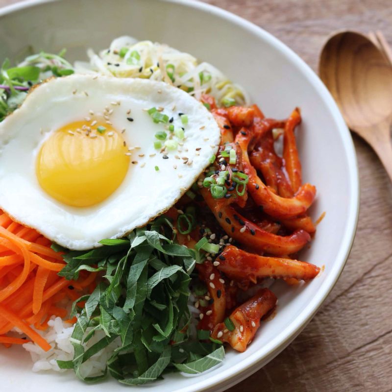 그릇에 밥을 담고 양념한 오징어, 콩나물, 깻잎, 새싹, 당근, 달걀프라이를 돌려 담아주세요. 마지막에 약간의 참기름과 통깨를 뿌려주세요.