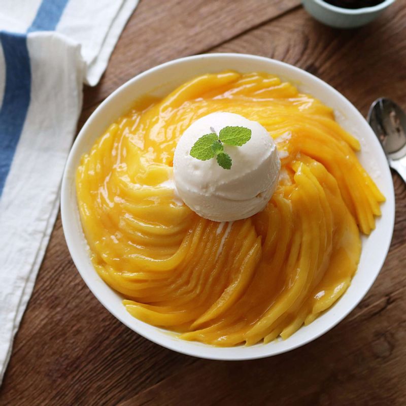 그릇에 갈린 우유얼음을 담고, 슬라이스한 망고를 돌려 담아주세요. 스쿱으로 아이스크림 퍼서 동그랗게 올리고 망고소스를 뿌린 후 민트잎(생략가능)을 장식으로 올려주세요.