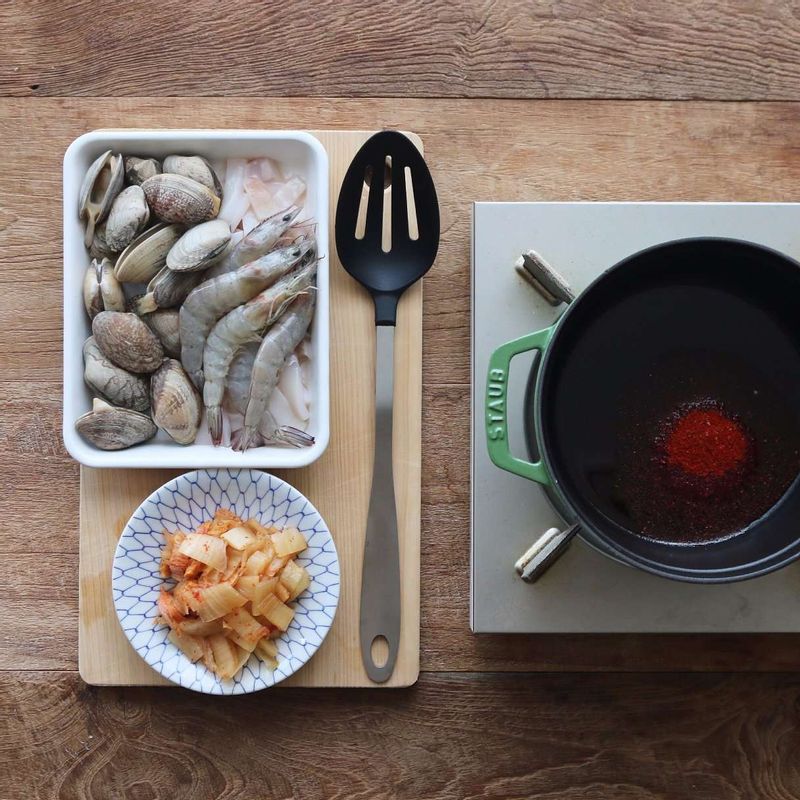 냄비에 고추기름과 고춧가루를 넣은 후 손질한 해물, 김치를 넣어 3분 정도 볶아주세요.