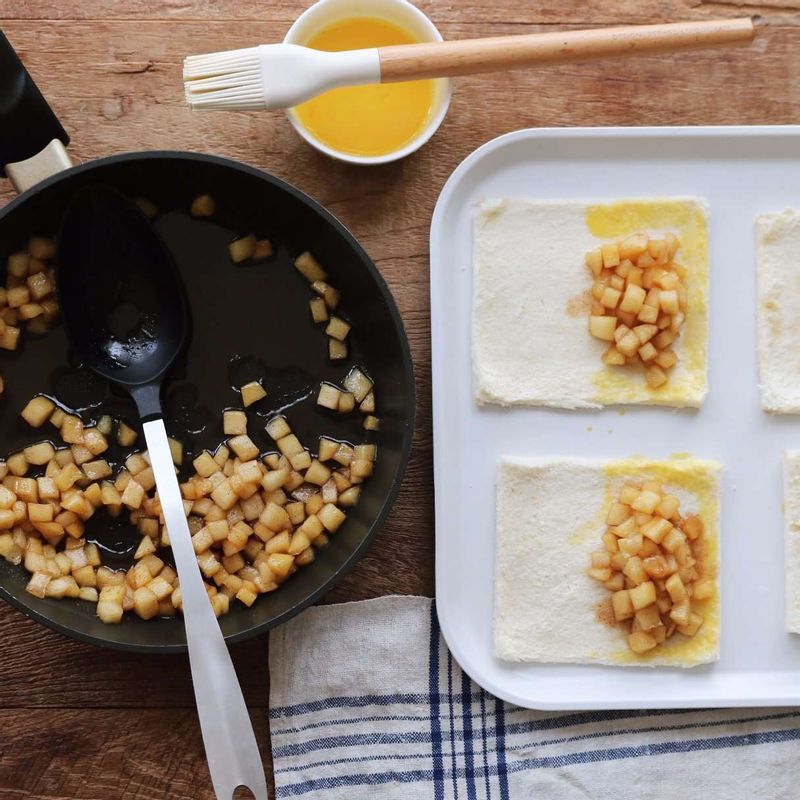 빵 한쪽면에 사과조림을 얹고, 식빵 테두리에 달걀물을 발라 접어주세요. 포크로 테두리를 눌러 양쪽면을 붙인 후 사과파이 중앙에 칼집을 넣어주세요.