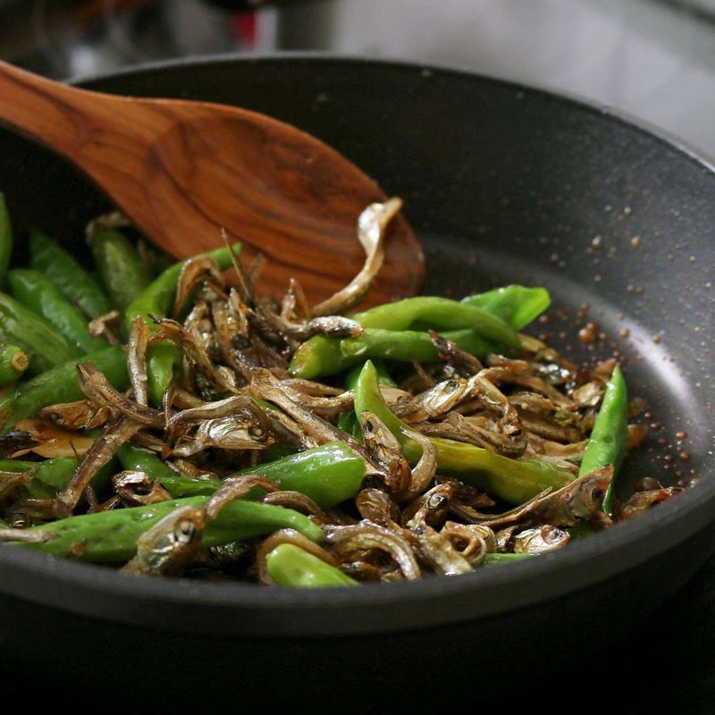 양념 재료와 꽈리고추, 멸치를 넣은 후 센불에서 2~3분간 더 볶아주세요. 홍고추, 참기름, 통깨를 넣고 고루 섞어 마무리해주세요.