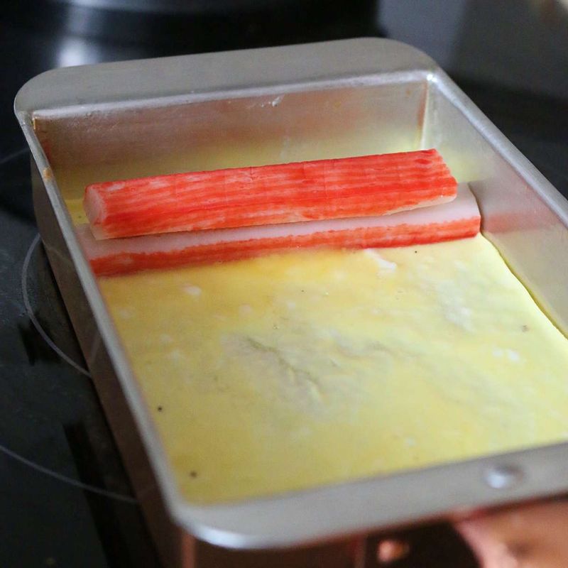 달군 팬에 식용유를 두르고 달걀물을 한 국자 넣은 후 팬 앞쪽에 맛살 두 개를 겹쳐서 올려주세요.