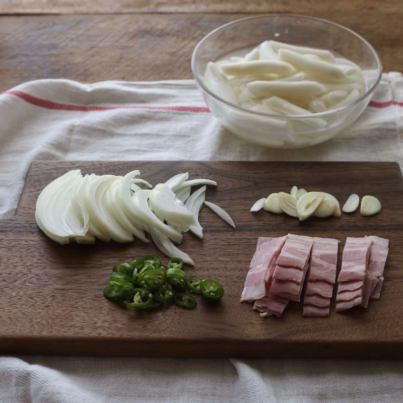 떡볶이떡은 찬물에 20분 정도 담갔다가 체에 밭쳐 물기를 빼주세요. 양파는 채썰고 베이컨은 먹기 좋은 크기로 썰어주세요. 청양고추는 송송썰고 마늘은 편으로 썰어주세요.