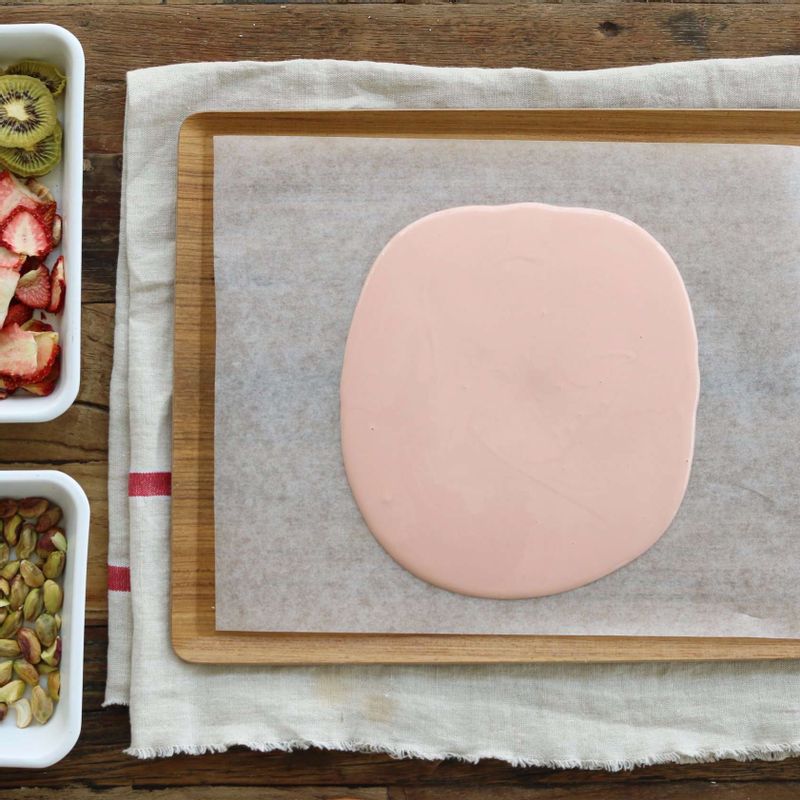 평평한 쟁반에 유산지를 깔고 녹인 초콜릿을 부어 고르게 편 후, 과일건조칩과 견과류를 올려주세요.