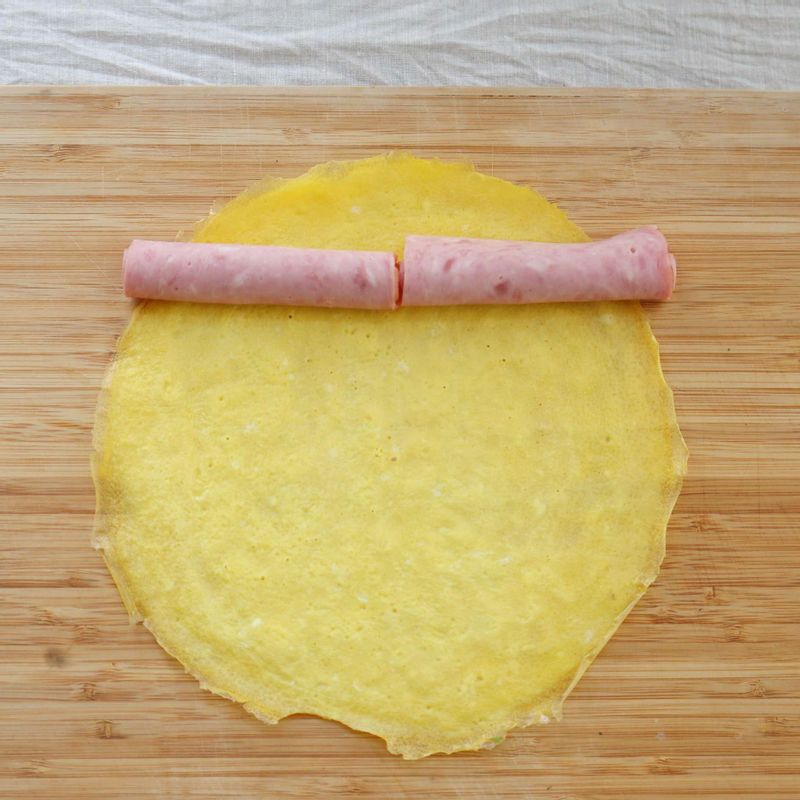 햄을 동그랗게 말아 지단 위에 올리고, 함께 돌돌 말아주세요.
