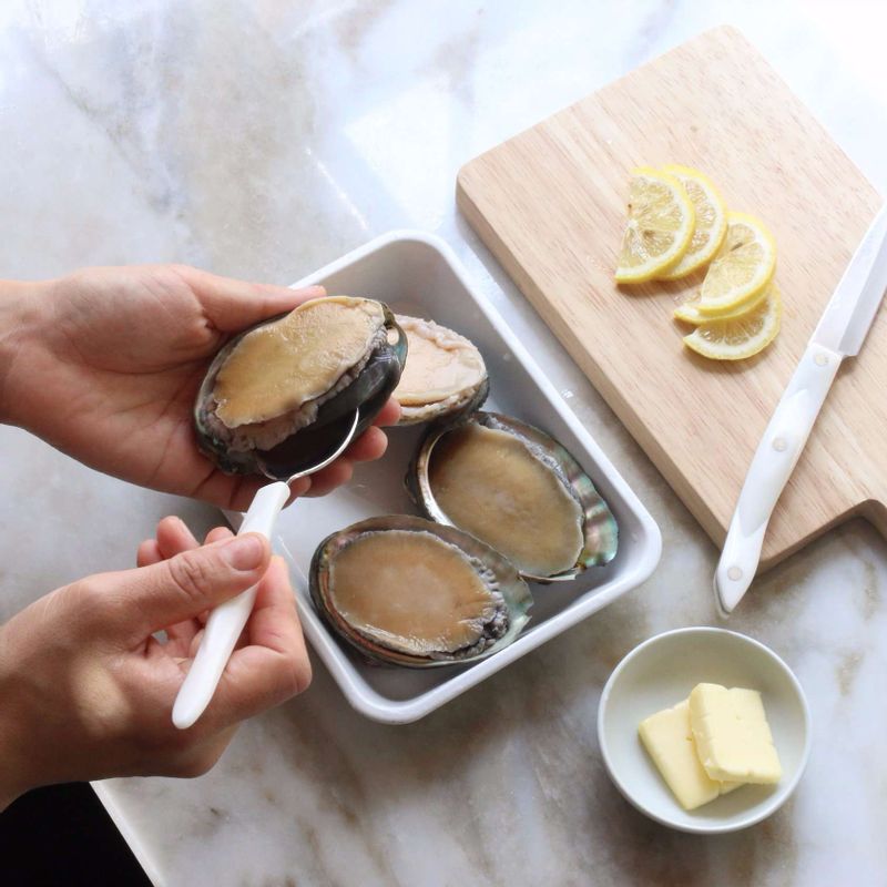 전복은 껍질과 살 사이에 숟가락을 넣어 살을 분리하고, 이빨과 내장을 제거해주세요. 레몬은 반달모양으로 얇게 썰어주세요.