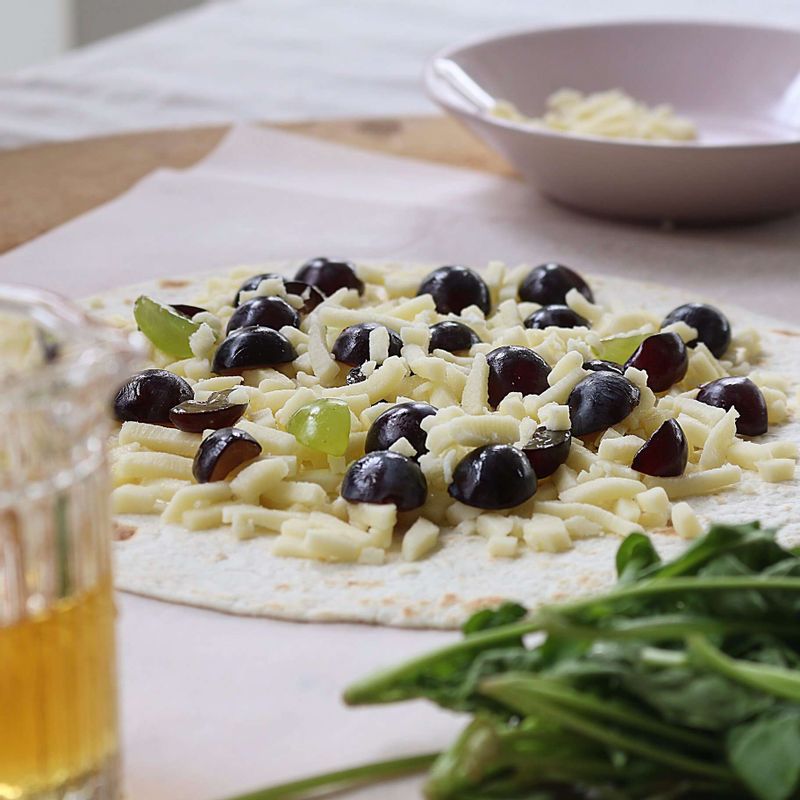 토르티야에 꿀 1큰술을 넓게 바르고, 피자치즈와 포도를 골고루 올려주세요.