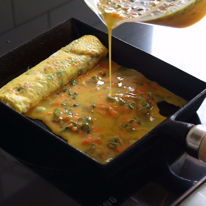 중약불로 달군 팬에 약간의 식용유를 두르고 달걀물을 국자로 떠서 넣은 후, 윗면이 반쯤 익으면 달걀을 돌돌 말아주세요.