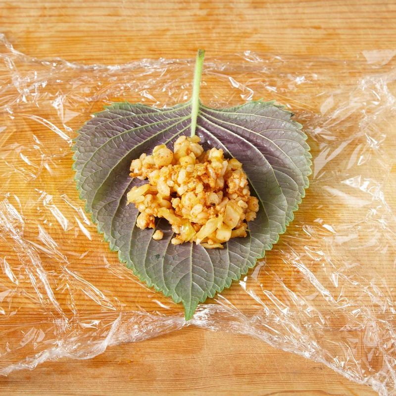 랩 위에 깻잎을 올리고 볶음밥을 올린 후 동그랗게 뭉쳐주세요.
(흩어지기 쉬운 재료이므로 랩을 이용해 모양을 잡고, 그대로 도시락에 싸 먹기 직전에 풀러 한입에 드세요.)