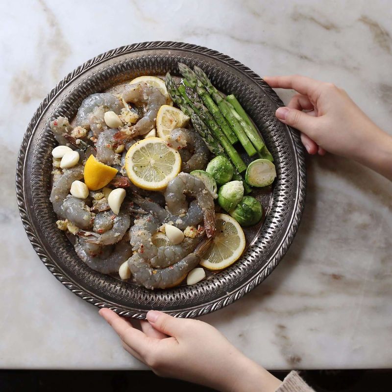 오픈 팬에 양념한 새우와 레몬, 마늘, 아스파라거스, 미니 양배추를 올린 후 야채에 올리브오일, 소금, 후춧가루를 뿌려 180도로 예열된 오븐에 넣어 15분 정도 구워주세요.
(에어프라이어를 사용할 때는 180도에서 10분, 뒤집어서 5분 정도 구워주세요.)