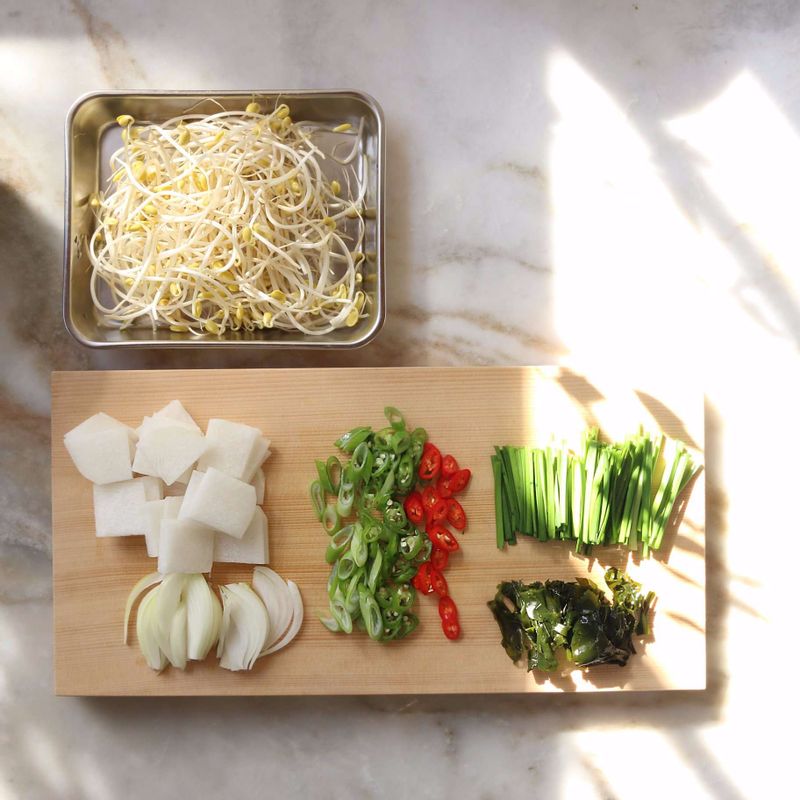 불린 미역은 먹기 좋은 크기로 자르고, 무는 나박썰기 해주세요. 대파와 청양고추, 홍고추는 어슷하게 썰어주세요. 양파는 채를 썰고 부추는 깨끗이 씻어 4센치 길이로 썰어주세요