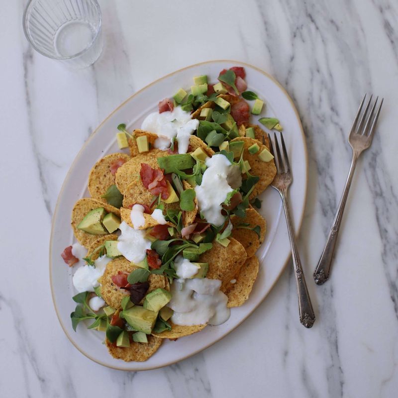 접시에 나초를 돌려 담고 베이컨, 아보카도를 올린 후 어린잎채소를 올려주세요. 샐러드에 올리브유와 후춧가루를 뿌려주세요.