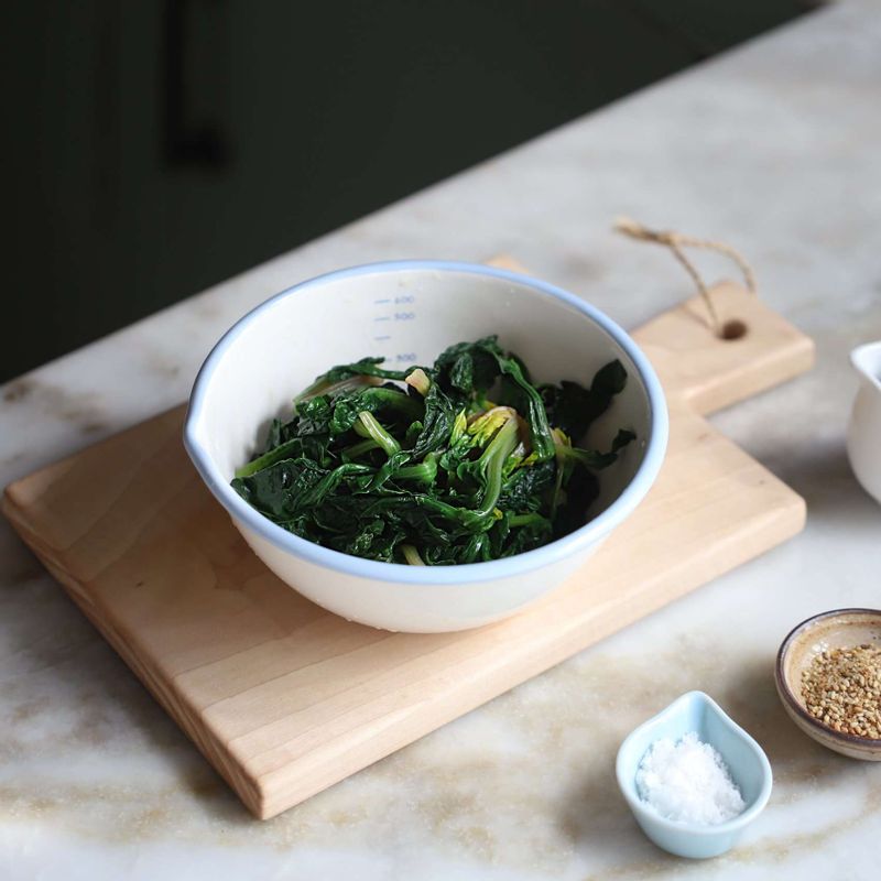 시금치는 뿌리를 자르고 깨끗이 씻고, 끓는 물에 약간의 소금을 넣어 살짝 데친 후 찬물에 헹궈서 물기를 제거해주세요. 데친 시금치에 약간의 소금과 참기름을 넣고 밑간 해주세요.