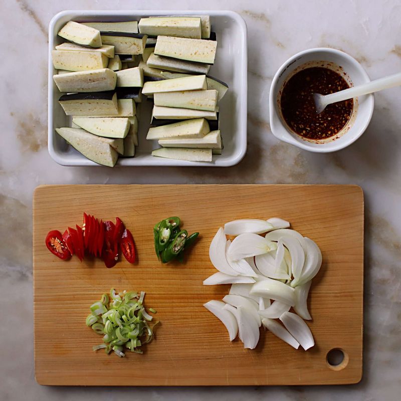 가지는 길이로 3등분 한 후 세로로 6등분해서 썰어주세요. 양파는 굵게 채를 썰고, 대파는 잘게 썰어주세요. 청양고추와 홍고추는 어슷하게 썰어주세요.