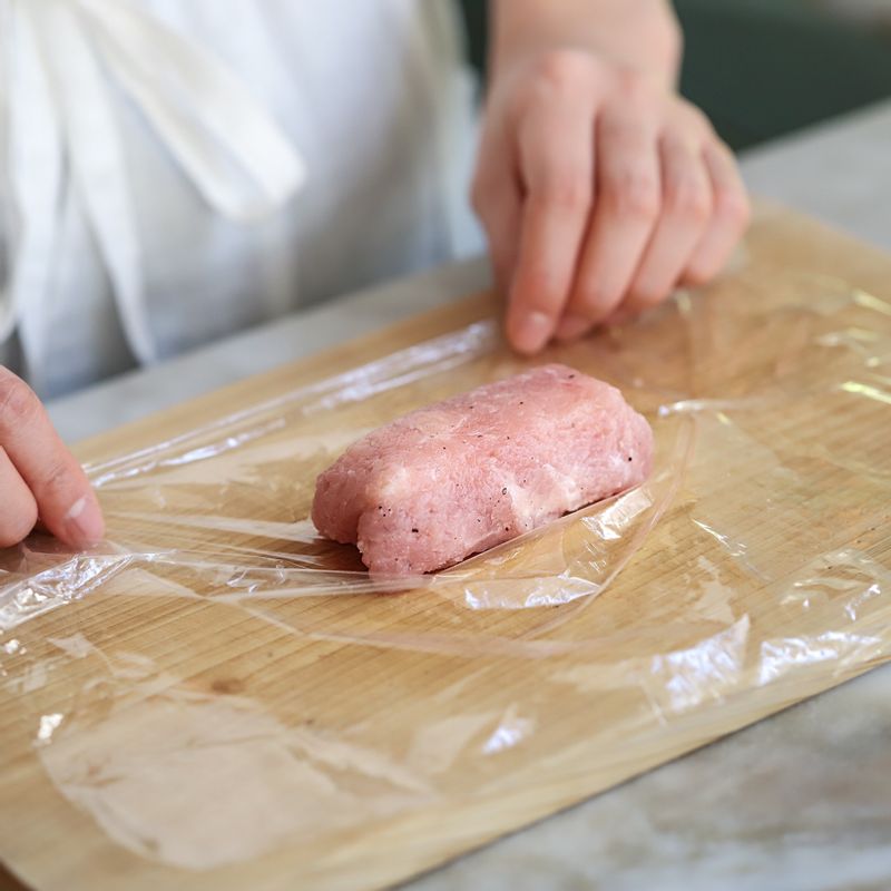 랩 위에 돼지고기를 평평하게 펴준 후 치즈를 올려주세요. 고기의 양옆을 접은 후 돌돌 말아 랩으로 모양을 고정시켜주세요.