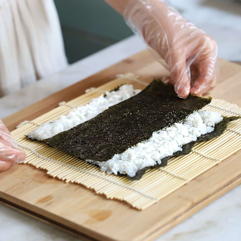 김발에 김을 올리고 밥을 고르게 편 후, 반으로 자른 김을 가운데에 깔고 준비한 재료와 우엉조림을 올려 김밥을 말아주세요.