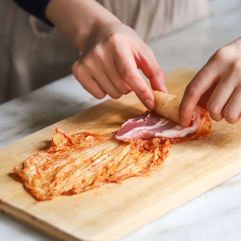 김치를 넓게 깔고, 삼겹살을 올려 돌돌 말아주세요.
