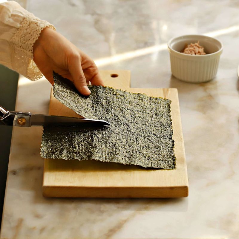 김밥용김은 2등분으로 잘라주세요. 밥을 적당한 크기로 동그랗게 뭉친 후 김밥용 김으로 감싸고 랩으로 한번 더 감싸서 단단하게 고정시켜주세요.