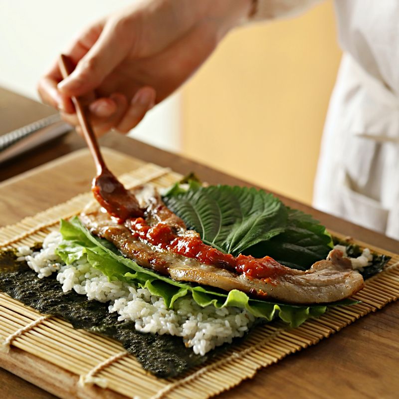 김발에 김을 올리고 밥을 고르게 편 후 청상추와 깻잎을 깔아주세요. 삼겹살과 준비한 재료, 쌈장을 넣은 후 김밥을 단단하게 말아주세요.
(기호에 따라 씻은 묵은지, 쌈무, 구운 마늘 등의 재료를 추가로 넣어 만들어 드셔도 맛있게 드실 수 있어요.)
(tip. 쌈장은 소스통이나 짤주머니에 넣어 사용하면 깔끔하게 넣을 수 있어요.)