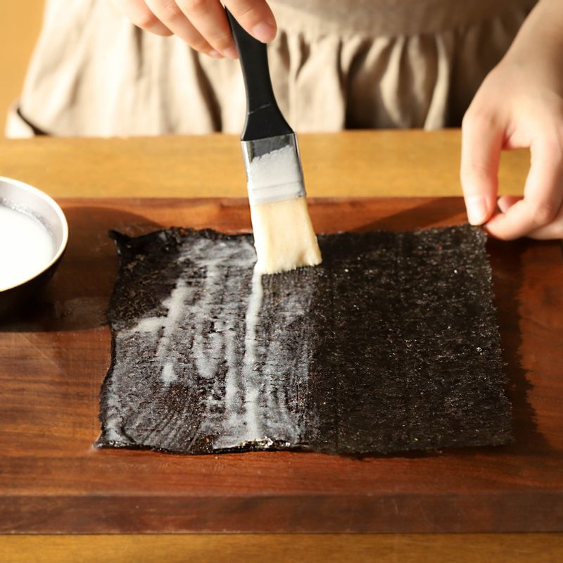 김의 거칠거칠한 부분 한쪽 면에 식힌 찹쌀풀을 얇게 펴 바르고 반으로 접어 한번 더 찹쌀풀을 발라준 후 먹기 좋게 통깨를 얹어주세요.
(tip 찹쌀 풀을 김의 가운데에서 바깥쪽으로 펴 가며 발라주면 김의 수축 현상을 줄 일 수 있어요.)